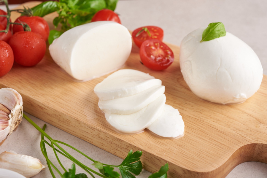 Fresh mozzarella balls and sliced mozzarella with basil and tomatoes, showcasing its fresh appeal.