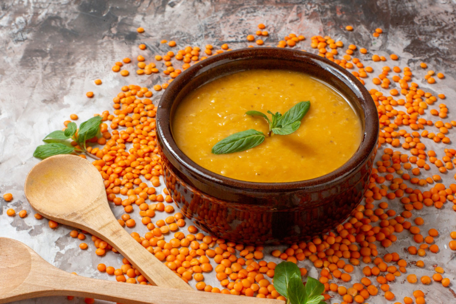 A bowl of rich, orange lentil soup with fresh herbs, surrounded by dry lentils.