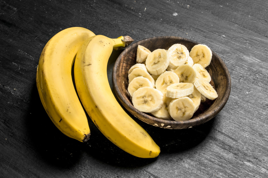 Whole bananas and sliced bananas in a wooden bowl, symbolizing quick energy.