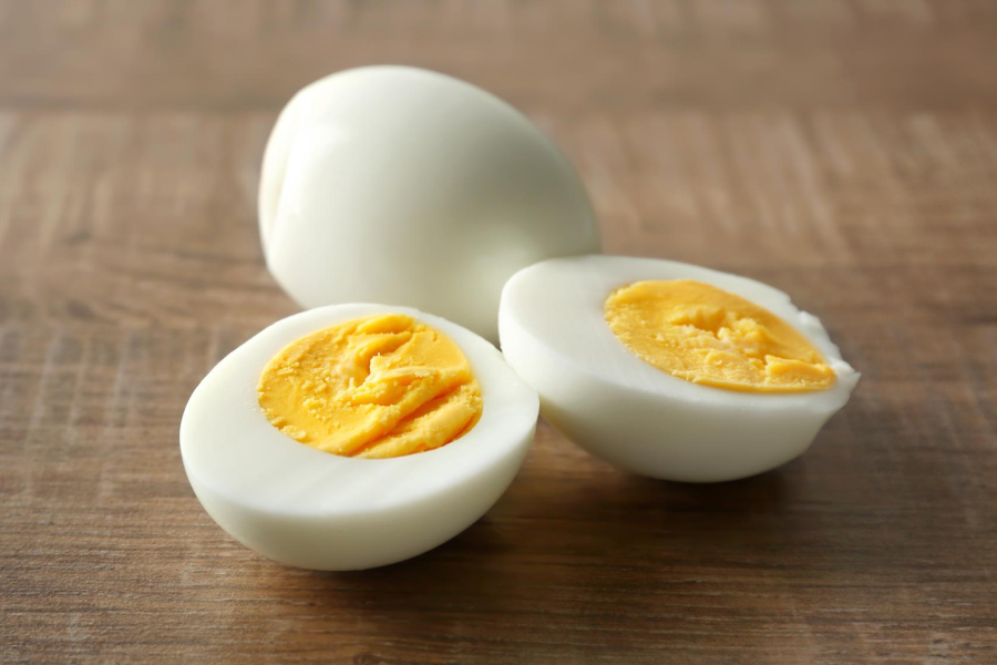 Peeled hard-boiled eggs on wood, one sliced open to show the yolk and white