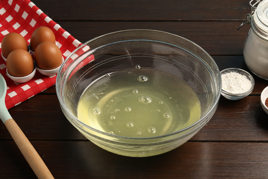A glass bowl of liquid egg whites next to whole brown eggs, showing the lean protein used in bodybuilding