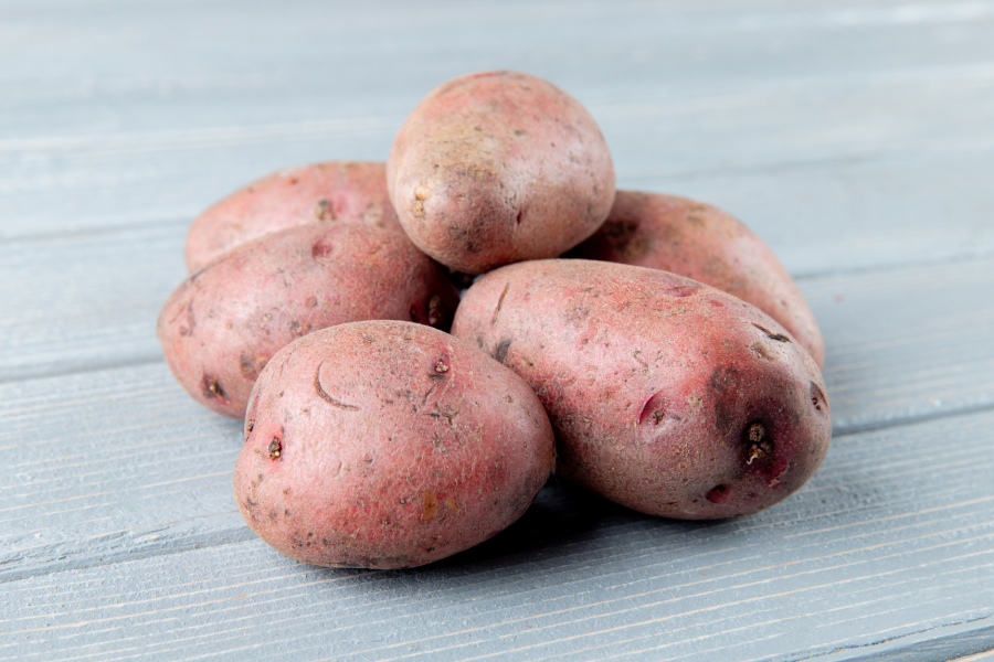 A close-up pile of unpeeled yellow and red potatoes, one sliced to show the interior